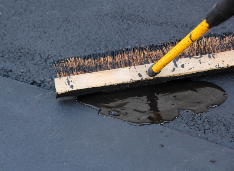 A broom smoothing out fresh asphalt on a road surface.