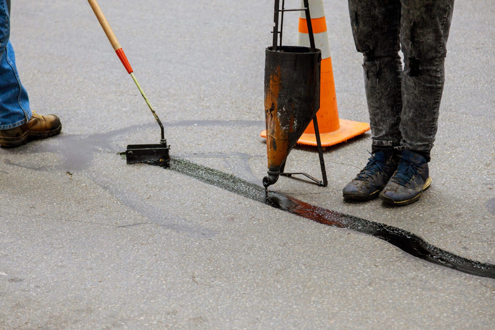 Worker filling a crack in concrete pavement with repair material.